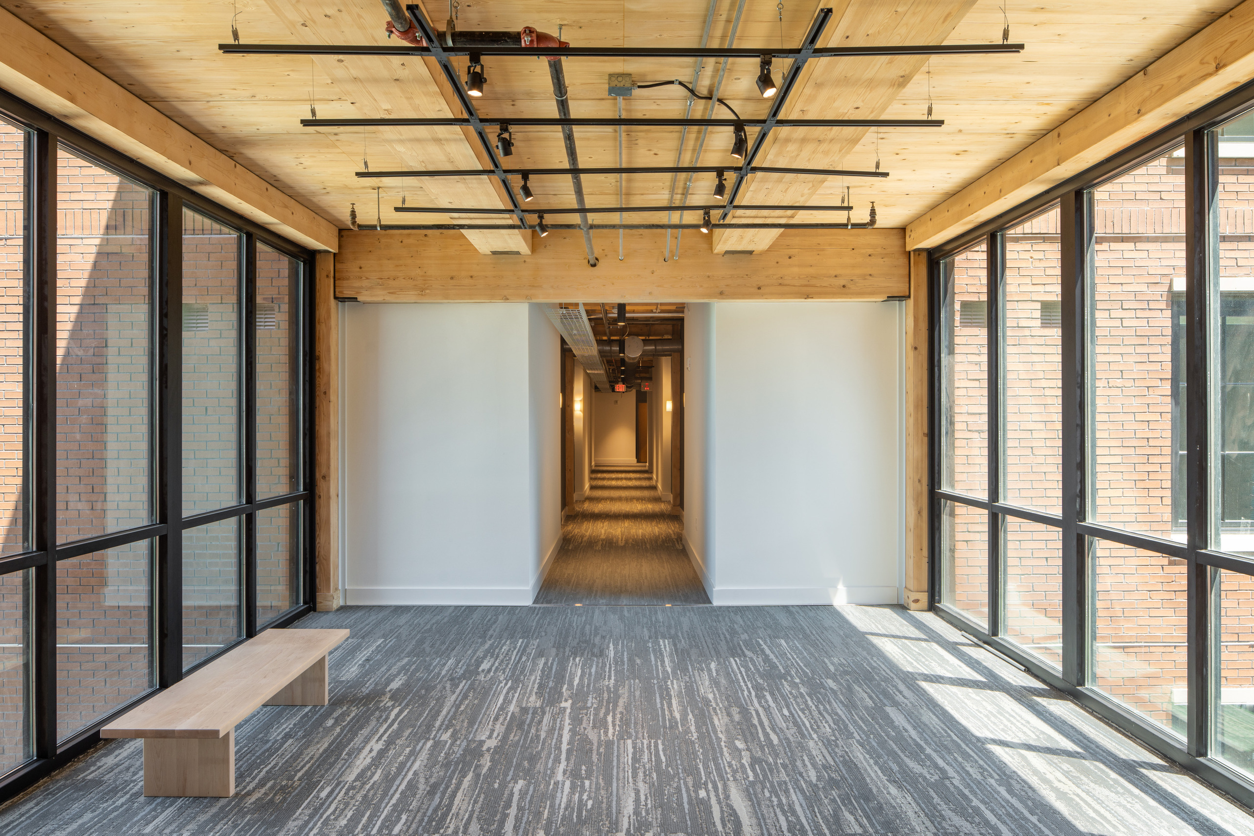 Glazed connector corridor at 111 Ann Street, with exposed mass-timber beams and brick wings visible through the windows.